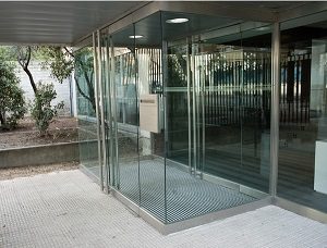 Felpudo metálico entre paneles de vidrio en edificio de oficinas